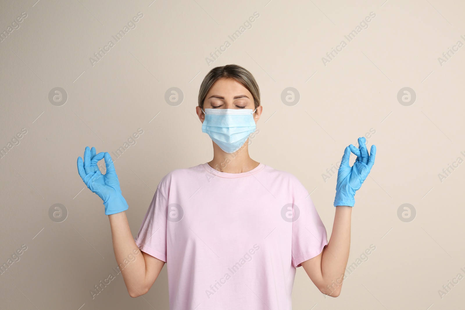 Photo of Woman in protective mask meditating on beige background. Dealing with stress caused by COVID‑19 pandemic