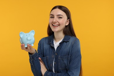 Photo of Happy woman with piggy bank on orange background