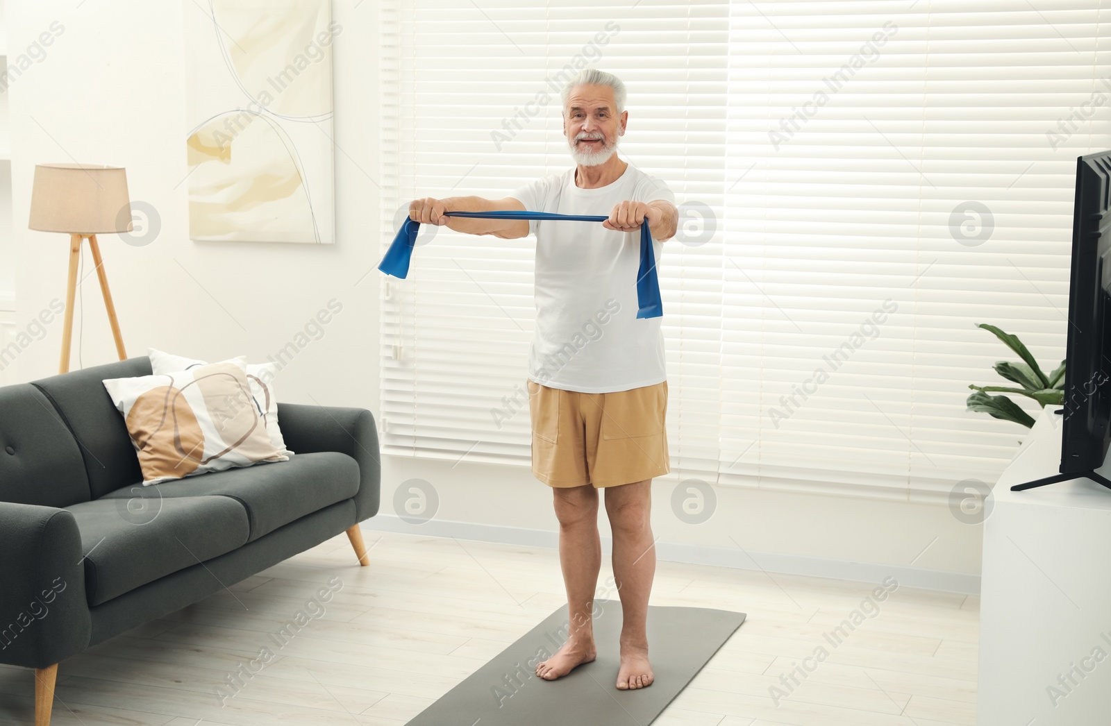 Photo of Senior man doing exercise with fitness elastic band on mat at home