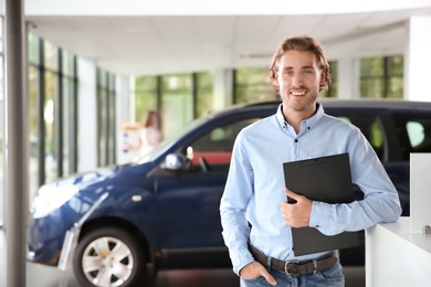 Photo of Salesman with clipboard near new car in modern auto dealership