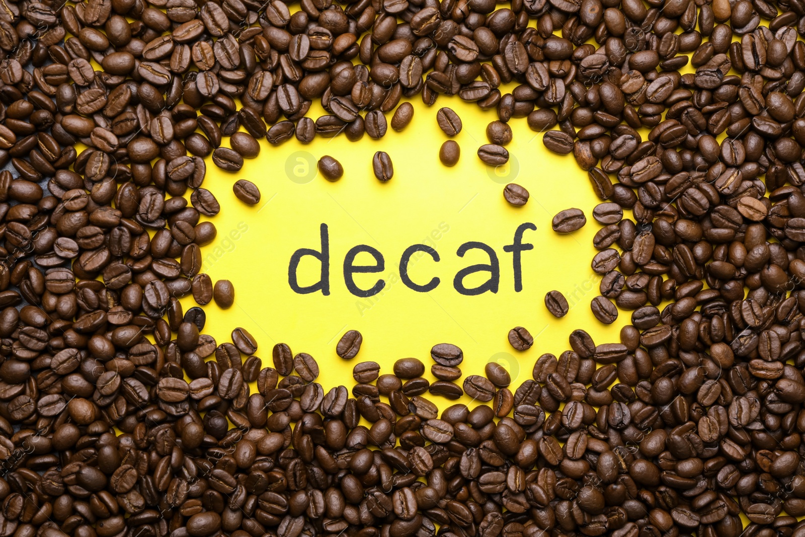 Photo of Word Decaf and coffee beans on yellow background, flat lay