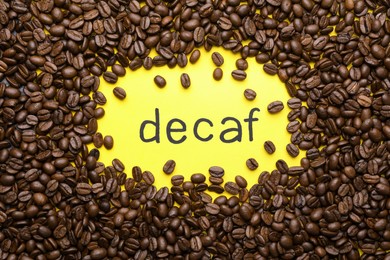 Photo of Word Decaf and coffee beans on yellow background, flat lay