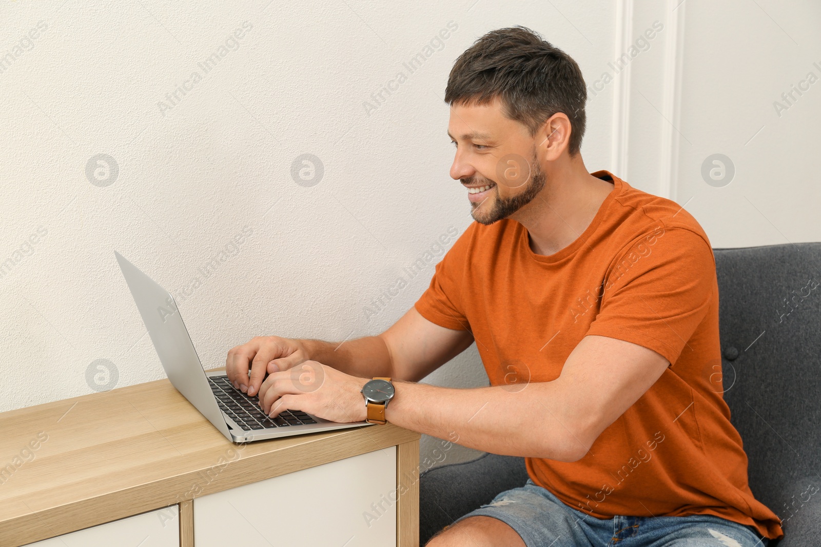 Photo of Happy man using laptop at table indoors. Internet shopping