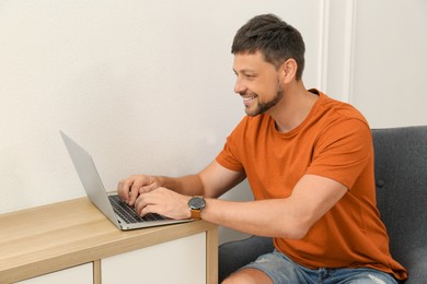 Happy man using laptop at table indoors. Internet shopping