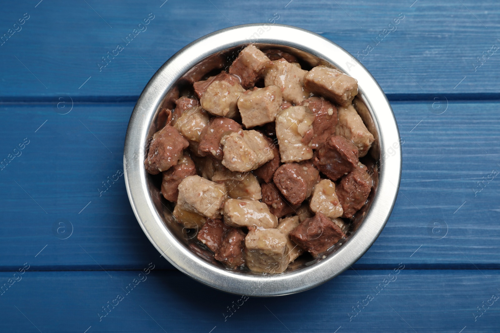 Photo of Wet pet food in feeding bowl on blue wooden table, top view
