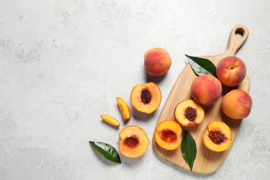 Delicious juicy peaches and leaves on light grey textured table, flat lay. Space for text