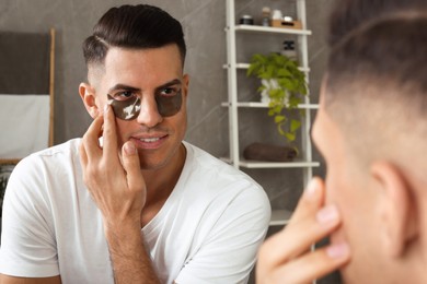Photo of Man applying dark under eye patches near mirror at home