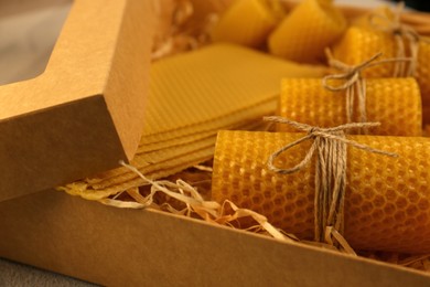 Photo of Beautiful yellow beeswax candles and sheets in box, closeup