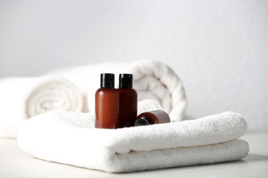 Photo of Mini bottles with cosmetic products and towels on table against light background. Hotel amenities