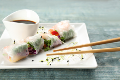 Photo of Delicious rolls wrapped in rice paper served on light blue wooden table