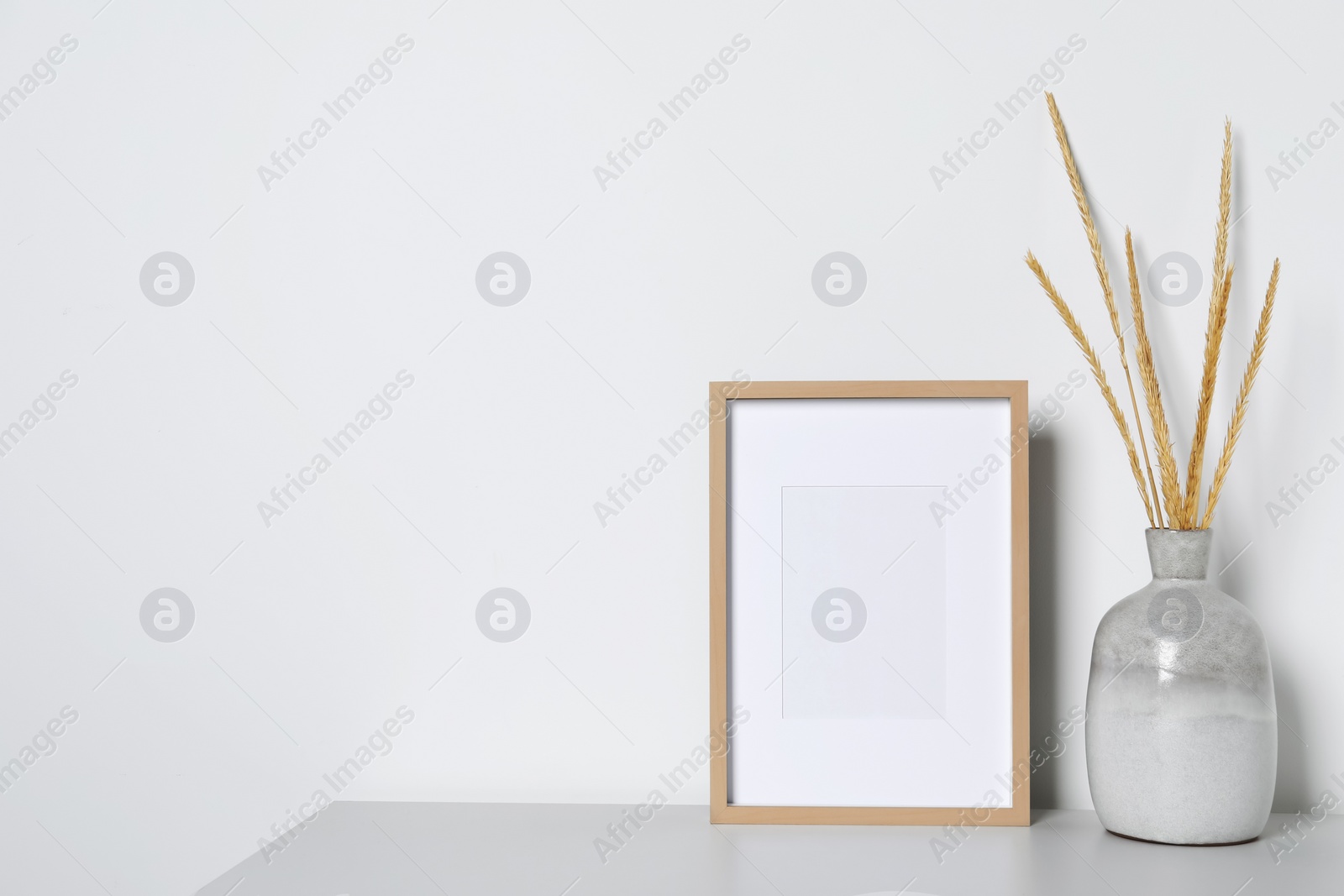 Photo of Empty photo frame and vase with dry decorative spikes on white table. Mockup for design