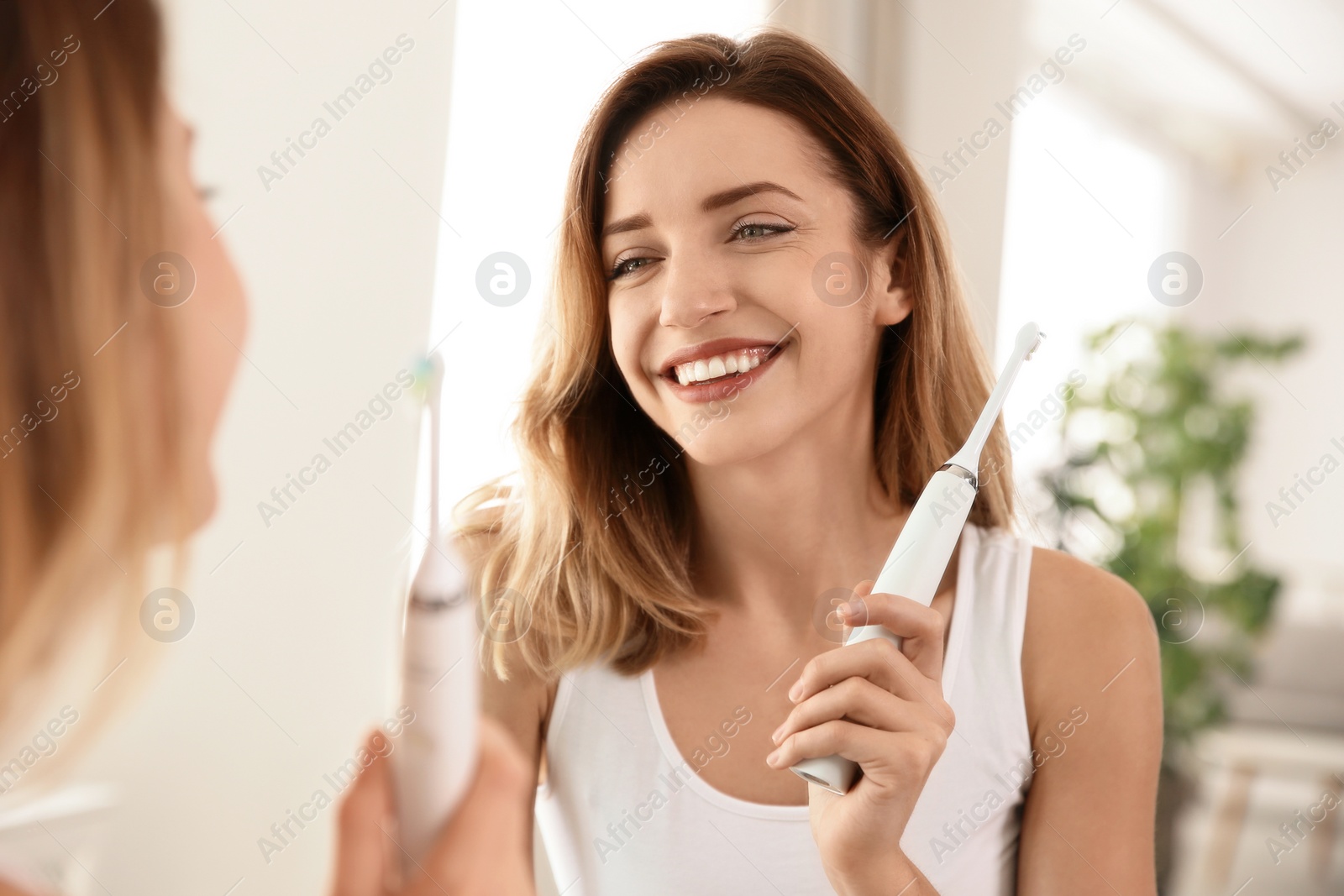 Photo of Young beautiful woman with toothbrush near mirror in bathroom. Personal hygiene