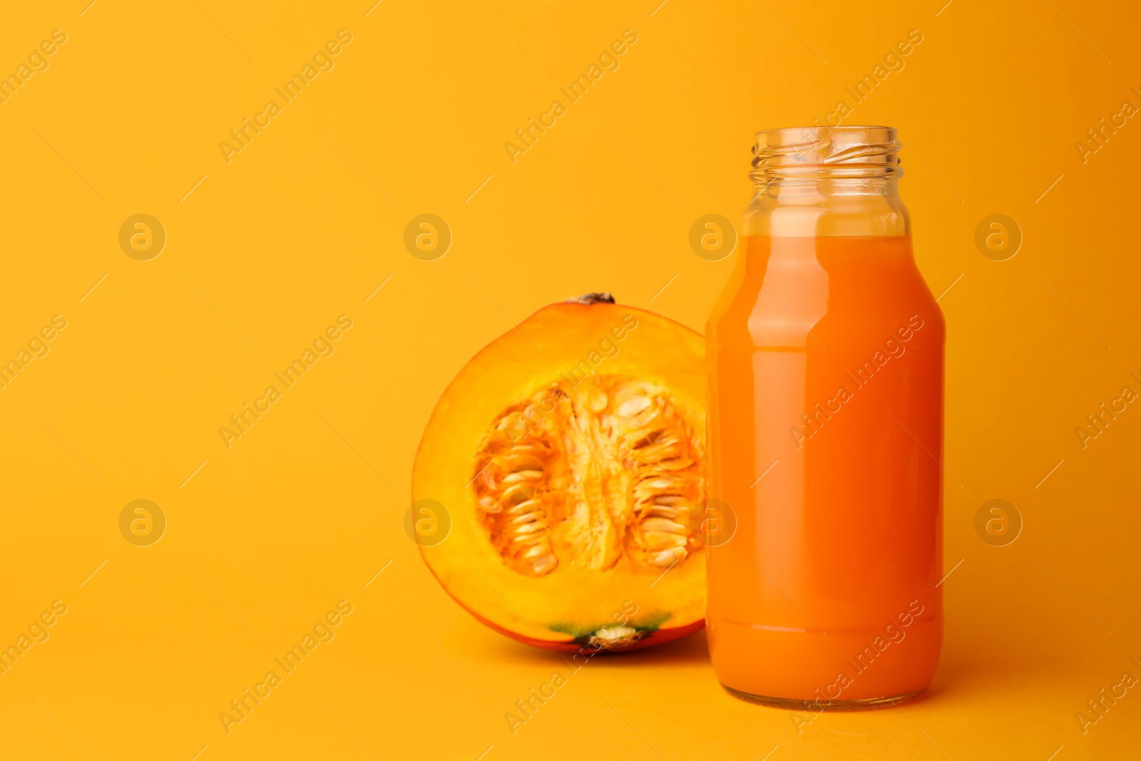 Photo of Tasty pumpkin juice in glass bottle and cut pumpkin on orange background. Space for text