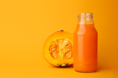 Tasty pumpkin juice in glass bottle and cut pumpkin on orange background. Space for text