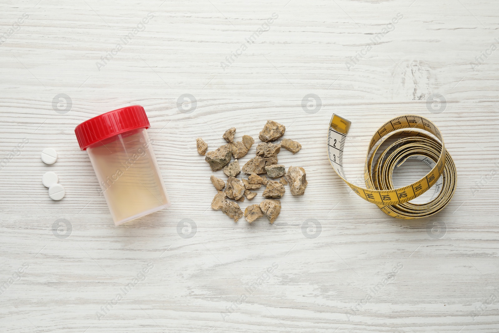 Photo of Kidney stones, jar of urine and measuring tape on white wooden table, flat lay