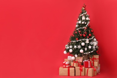 Photo of Christmas tree and gift boxes on red background, space for text