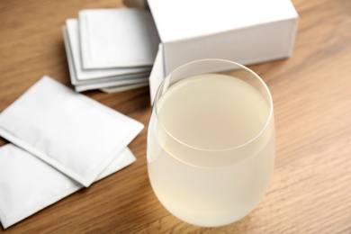 Medicine sachets and glass of water on wooden table