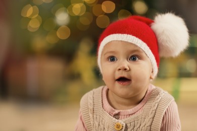 Photo of Cute little baby and blurred Christmas lights on background, space for text. Winter holiday