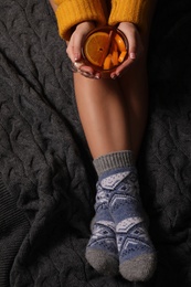 Woman in warm socks with cup of tea resting on knitted blanket, top view