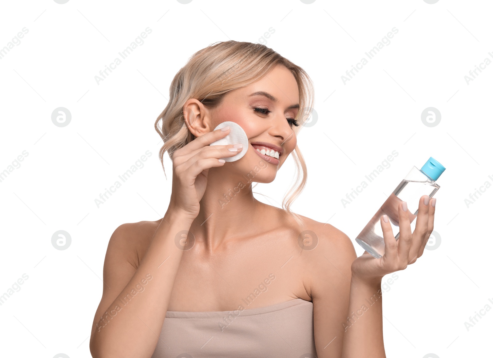 Photo of Smiling woman removing makeup with cotton pad and holding bottle on white background