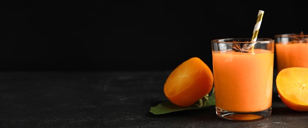 Tasty persimmon smoothie with anise and fresh fruits on black table, space for text. Banner design