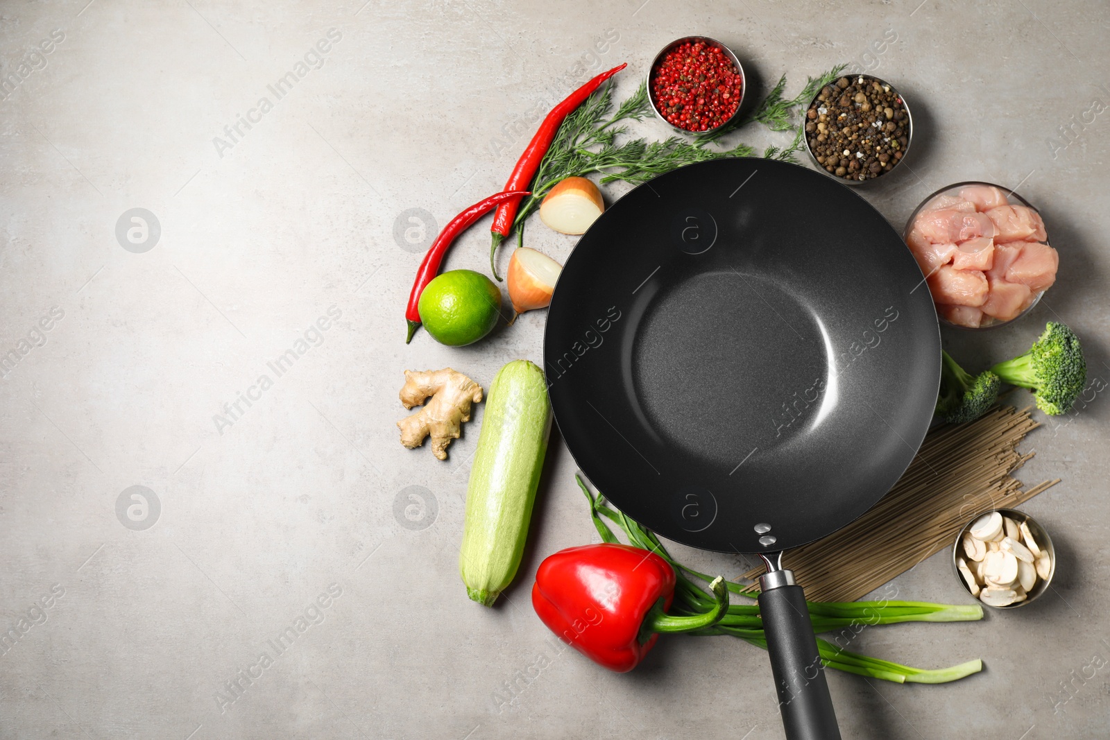 Photo of Empty iron wok surrounded by raw ingredients on grey table, flat lay. Space for text