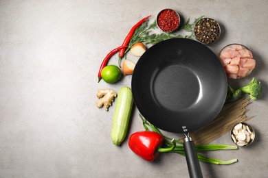 Empty iron wok surrounded by raw ingredients on grey table, flat lay. Space for text