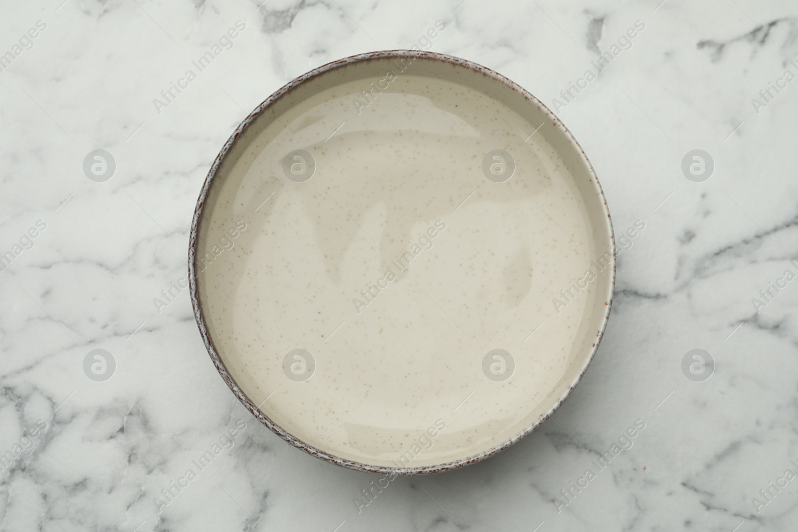 Photo of Beige bowl with water on white marble table, top view