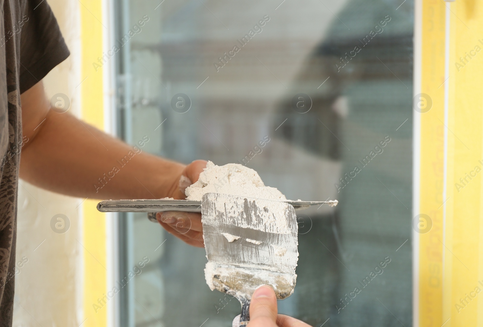 Photo of Professional worker with putty knifes and plaster near window indoors, closeup. Interior repair