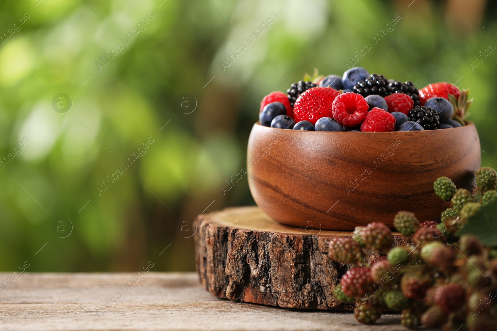 Photo of Different fresh berries in bowl on wooden table outdoors. Space for text