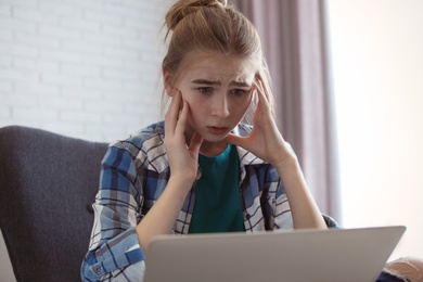 Photo of Shocked teenage girl with laptop indoors. Danger of internet