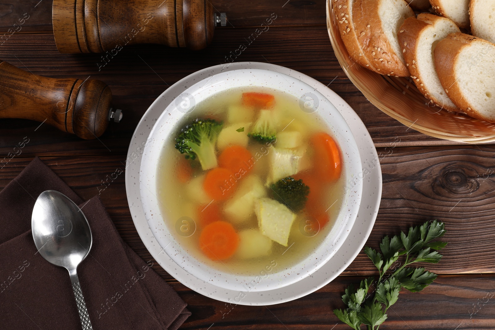 Photo of Tasty chicken soup with vegetables in bowl served on wooden table, flat lay