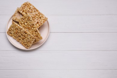 Photo of Delicious peanut bars (kozinaki) on white wooden table, top view. Space for text