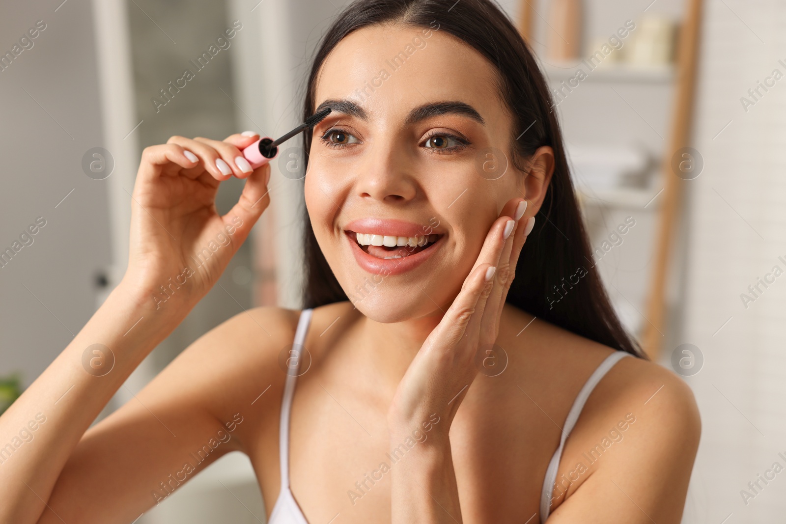 Photo of Beautiful young woman applying mascara indoors, closeup