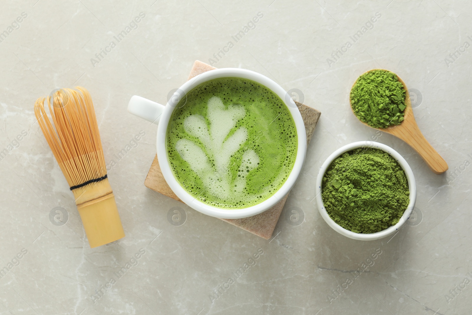Photo of Cup of fresh matcha latte, powder and bamboo whisk on light grey marble table, flat lay