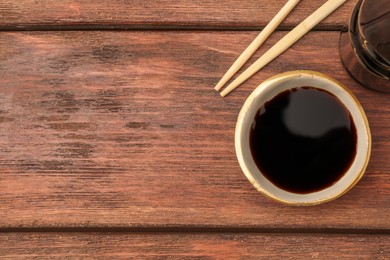 Bowl with soy sauce and chopsticks on wooden table, top view. Space for text