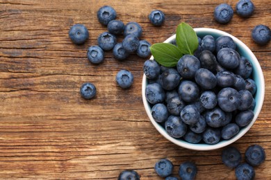 Photo of Tasty fresh blueberries and green leaves on wooden table, flat lay. Space for text