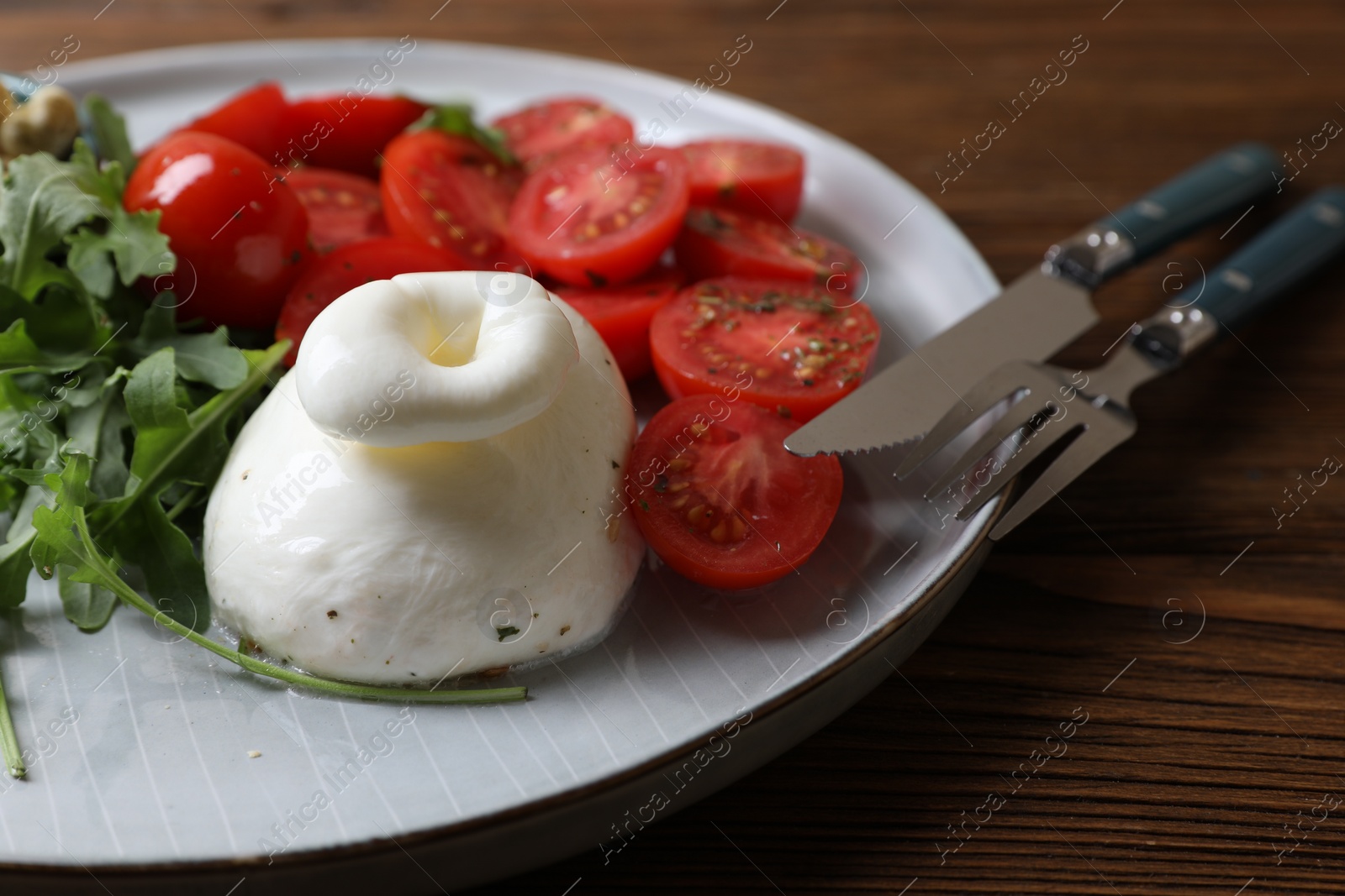 Photo of Delicious burrata cheese with tomatoes and arugula served on wooden table, closeup