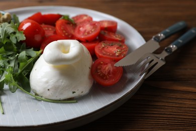 Delicious burrata cheese with tomatoes and arugula served on wooden table, closeup