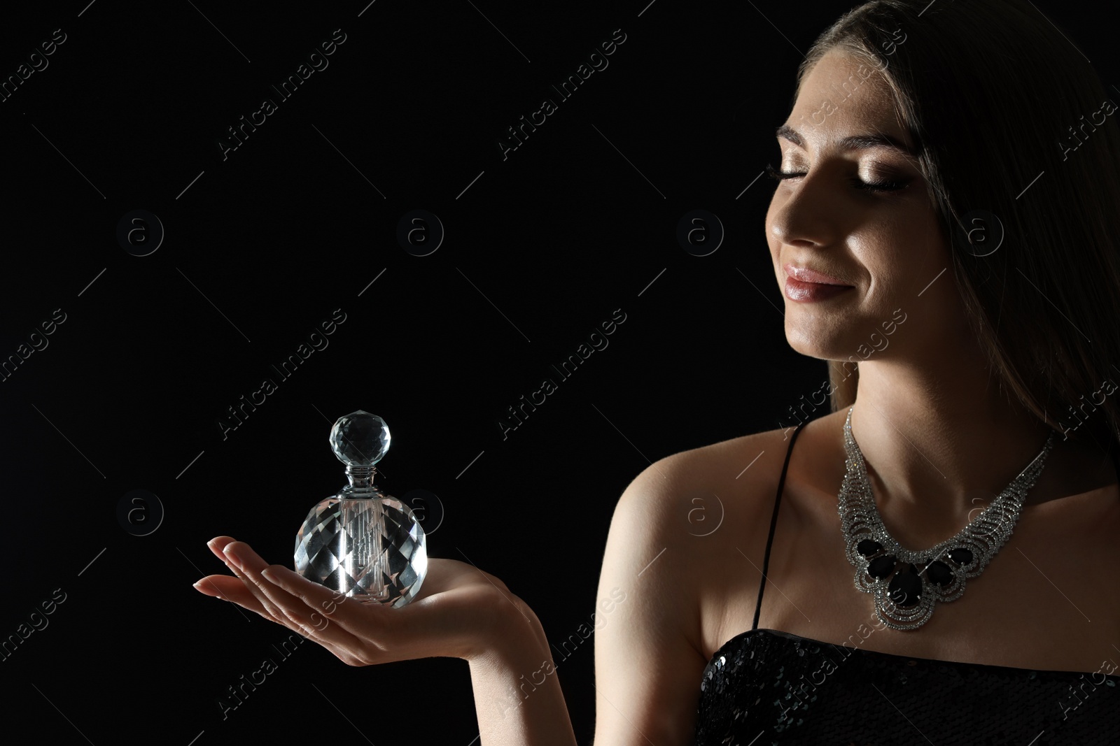 Photo of Young woman with bottle of perfume on black background. Space for text