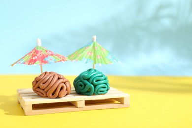 Photo of Brains made of plasticine on mini wooden sunbed under umbrellas against color background, space for text