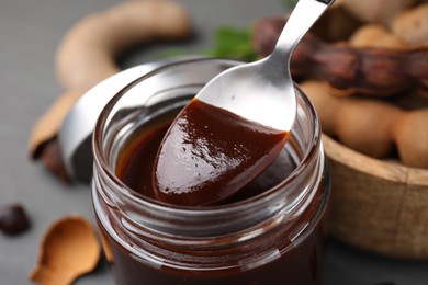 Photo of Taking tasty tamarind sauce with spoon from jar on table, closeup