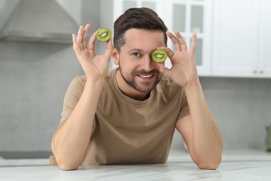 Man holding halves of tasty kiwi in kitchen