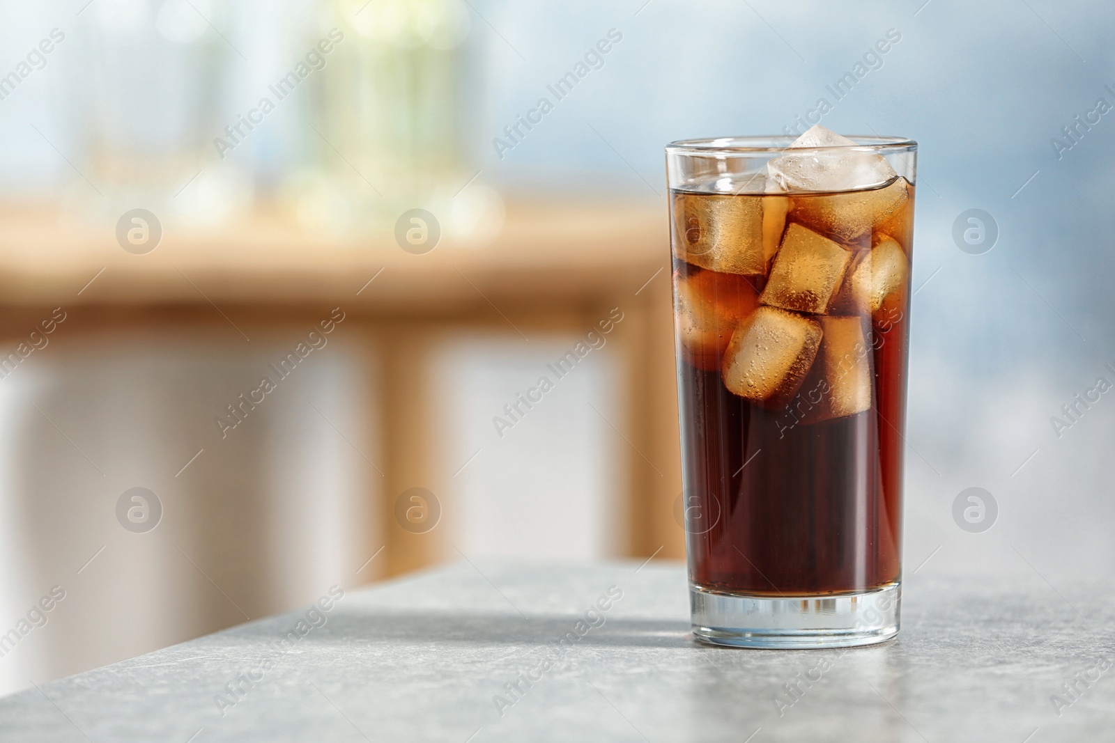 Photo of Glass of cold cola on table against blurred background. Space for text