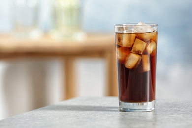 Glass of cold cola on table against blurred background. Space for text