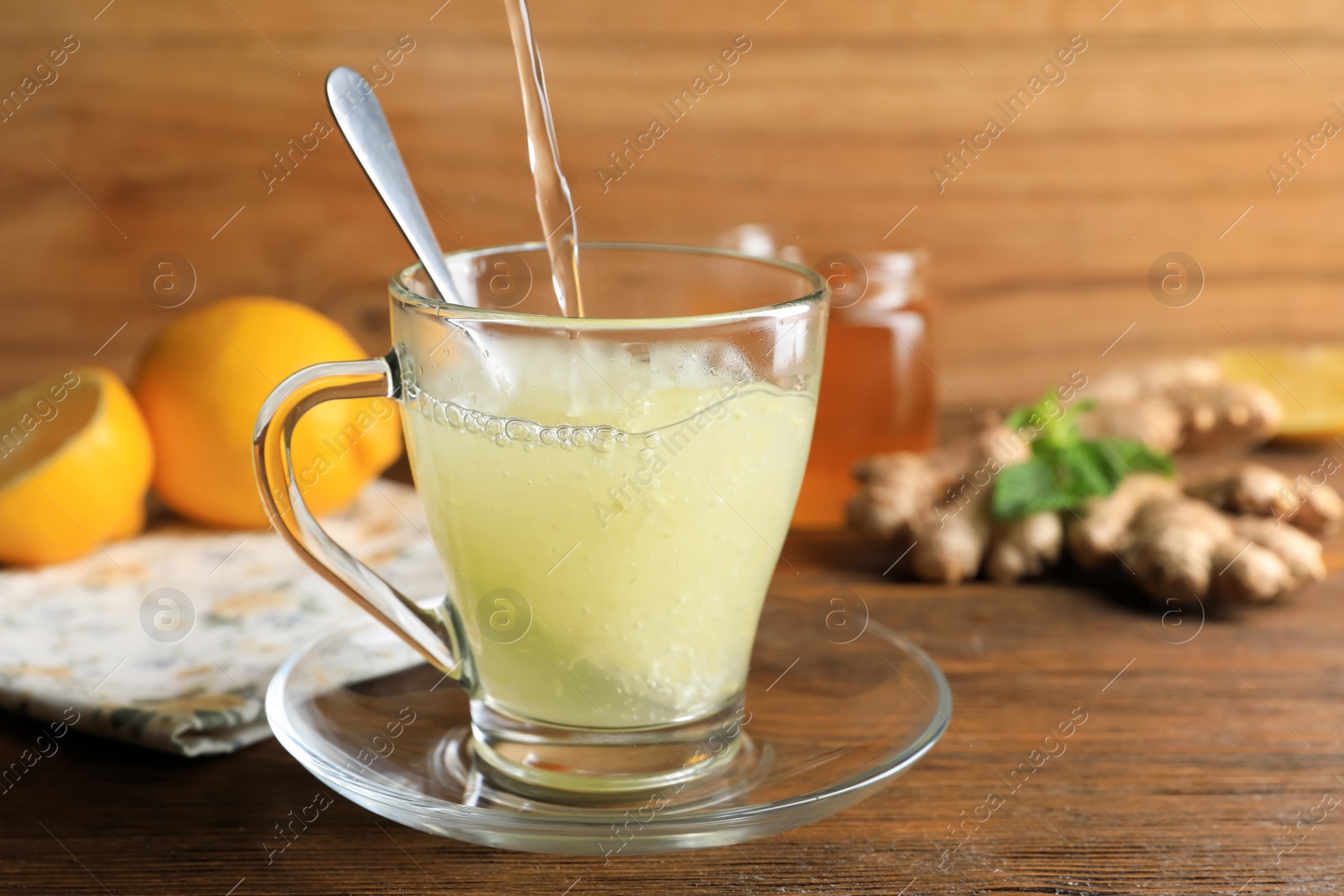 Photo of Pouring hot water into glass cup with grated ginger on wooden table