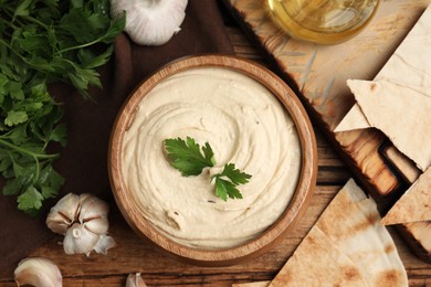Photo of Delicious hummus with pita chips and parsley on wooden table, flat lay