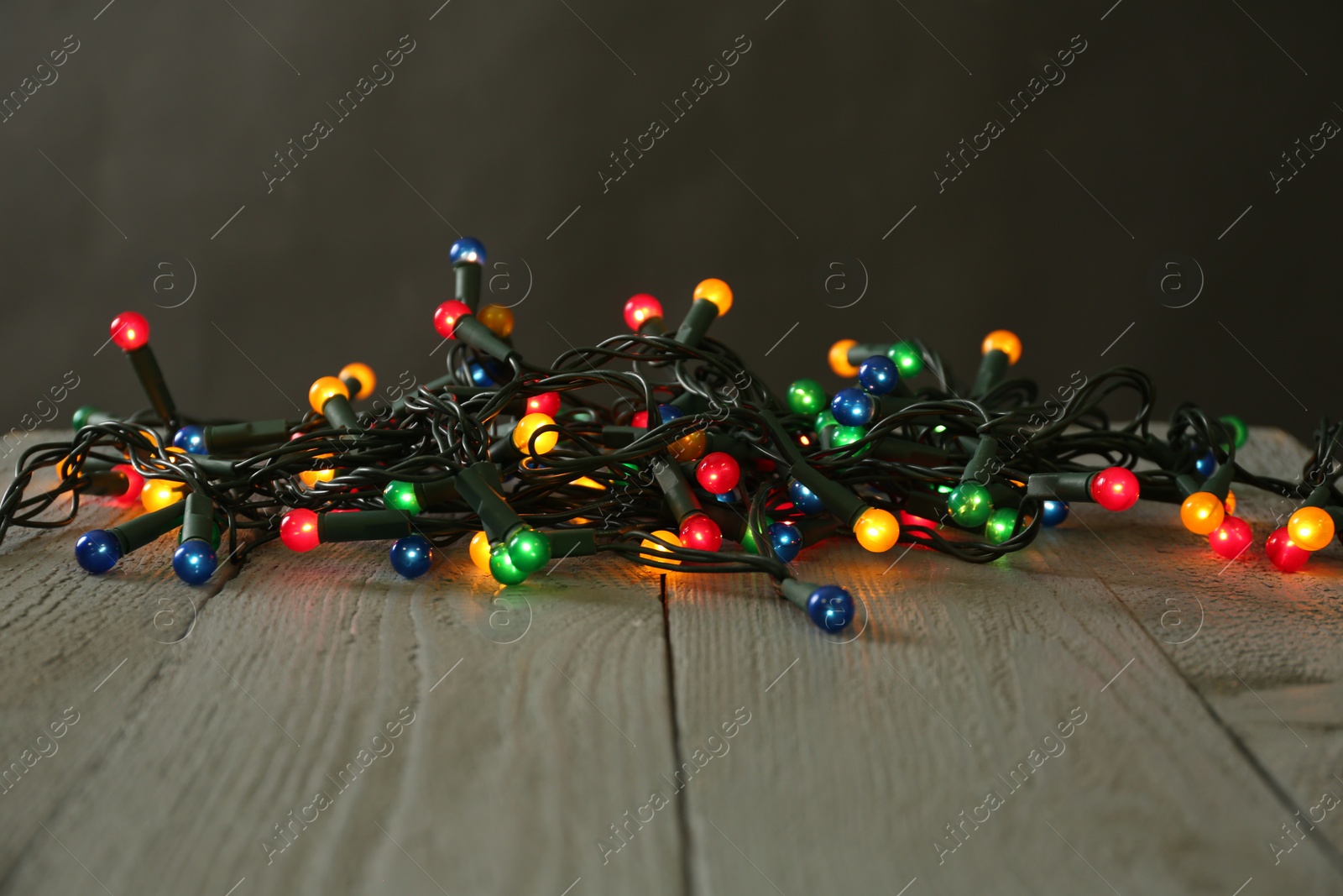 Photo of Beautiful glowing Christmas lights on wooden table against black background