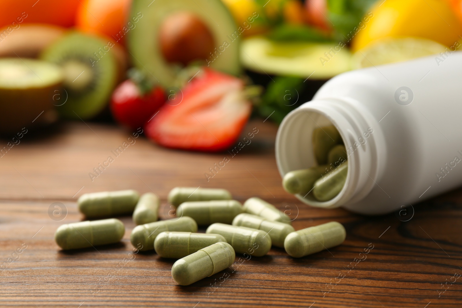 Photo of Vitamin pills, bottle and fresh fruits on wooden table, closeup