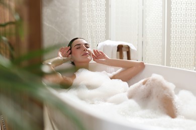 Beautiful young woman taking bubble bath at home